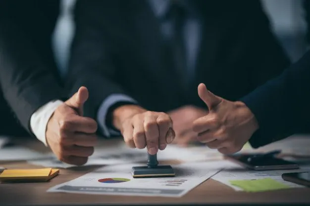 Two professionals giving a thumbs up over financial documents and charts on a desk